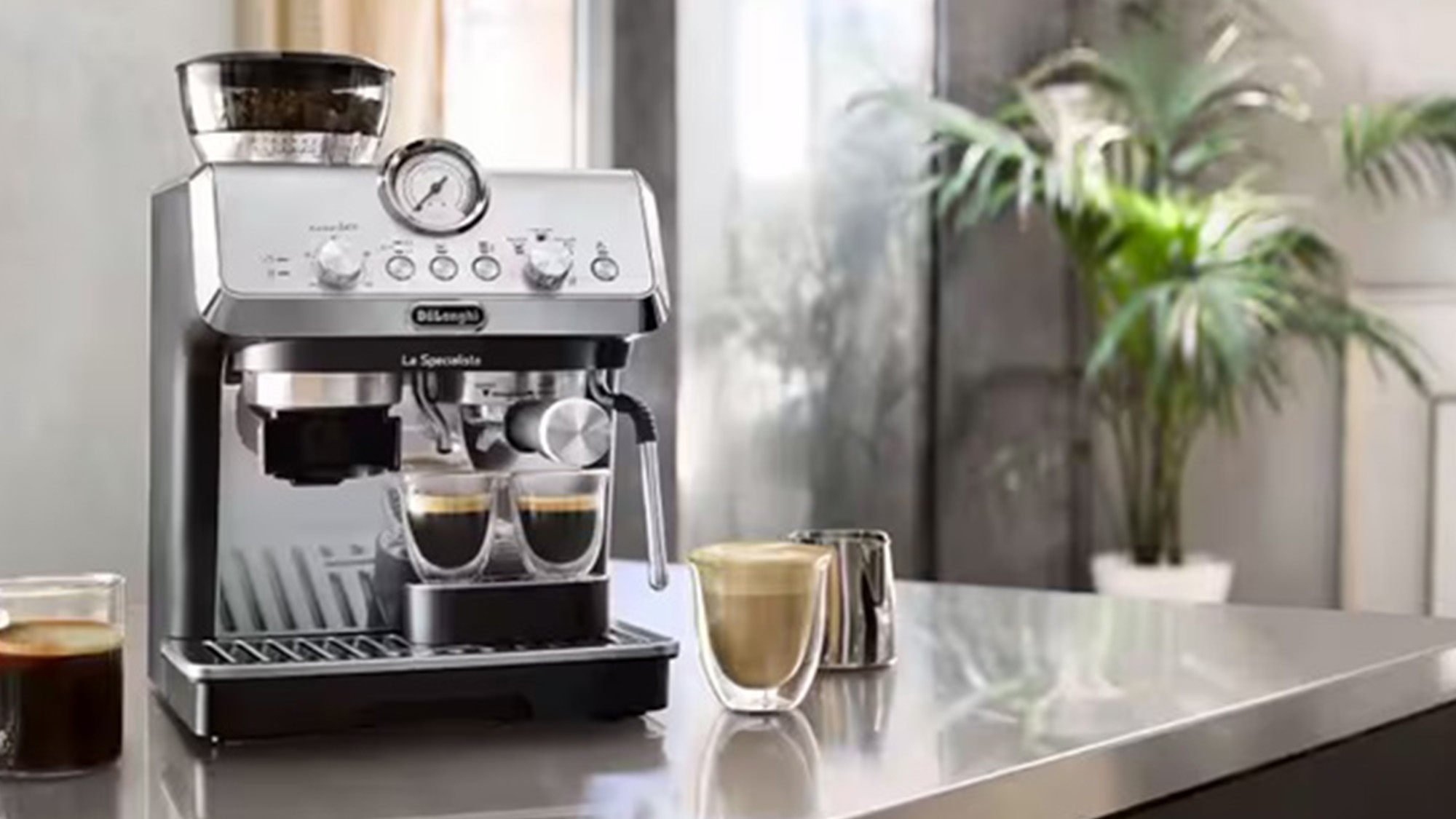 DeLonghi espresso machine on kitchen counter with fresh coffee in glass cups and potted plant by bright window