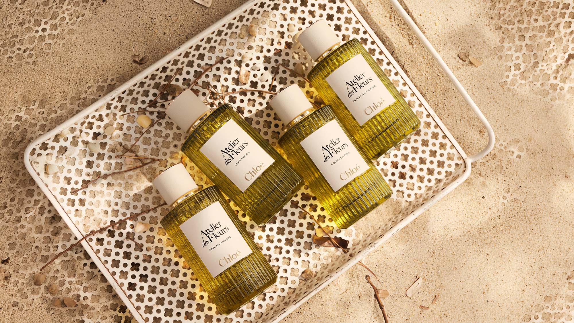 Four Atelier des Fleurs fragrance bottles by Chloé displayed on textured tray with dried botanicals
