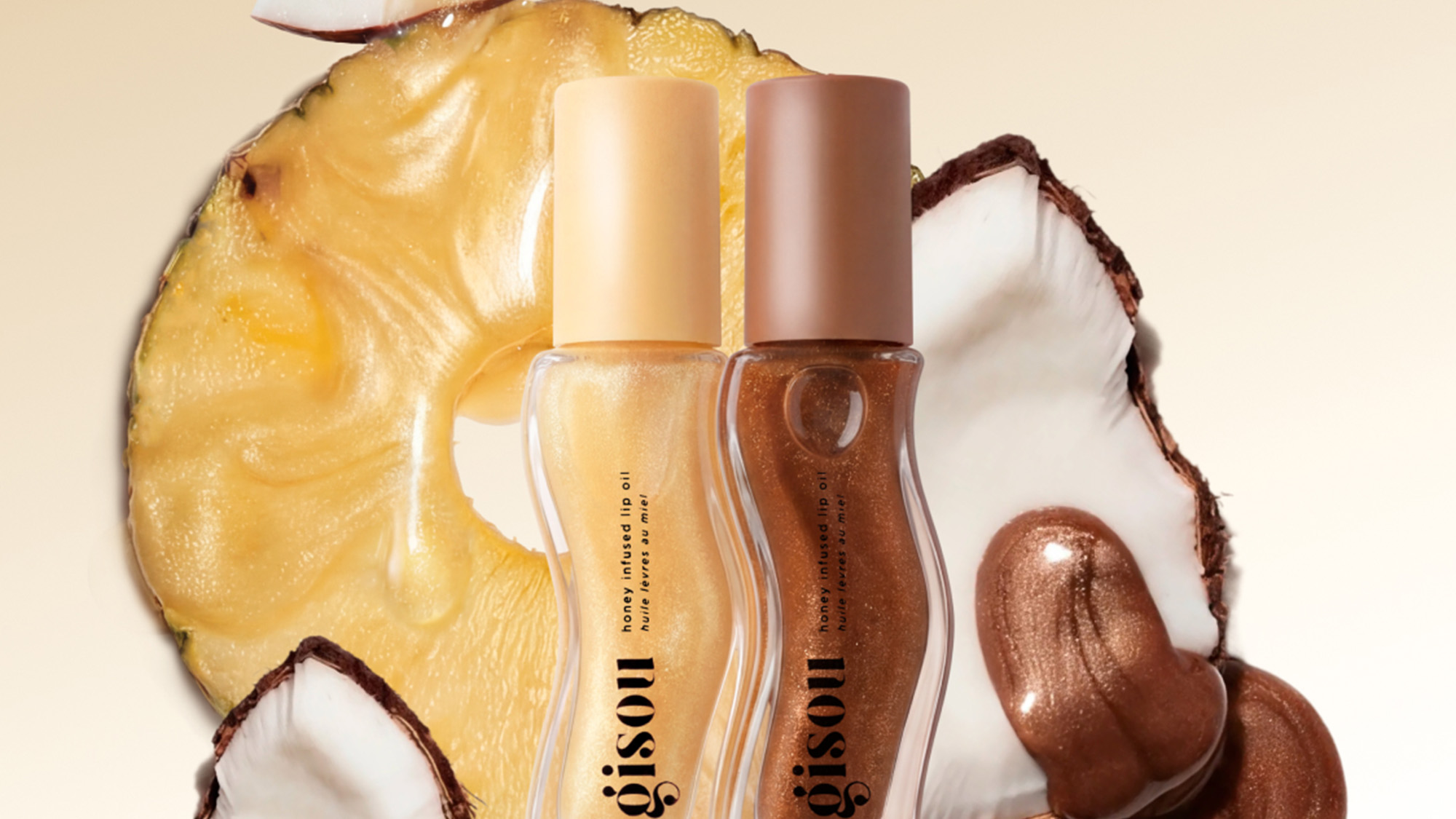Two honey infused lip oil bottles with pineapple and coconut elements on beige background