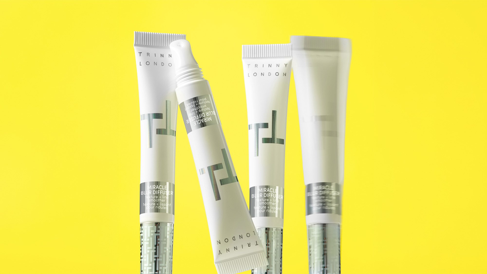 Four Trinny London Miracle Blur diffuser products in white and green packaging displayed on bright yellow background