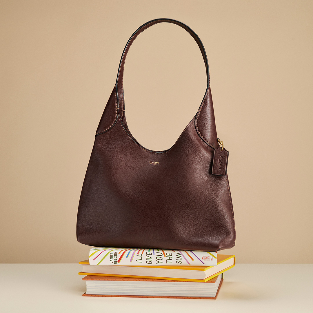 Burgundy leather Coach hobo bag displayed on stacked books with beige background