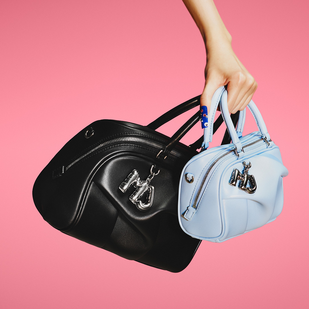 Hand holding black and light blue Marc Jacobs dome bags against pink background