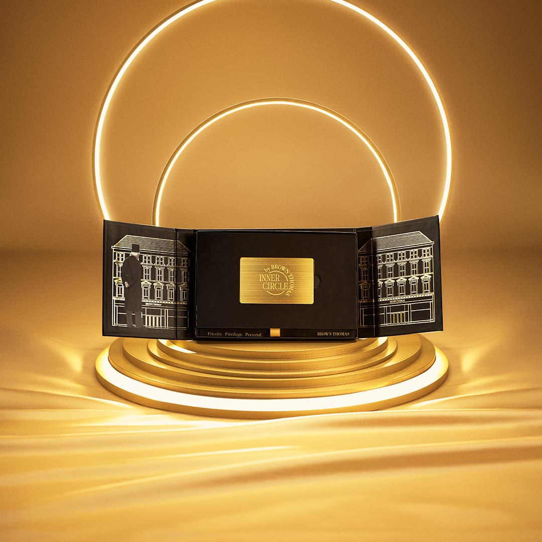 A sleek, black box with intricate gold designs and the words 'Inner Circle' is displayed open, revealing a luxurious presentation. It sits on an illuminated, golden circular platform, with glowing rings in the background, set against a warm, golden backdrop.