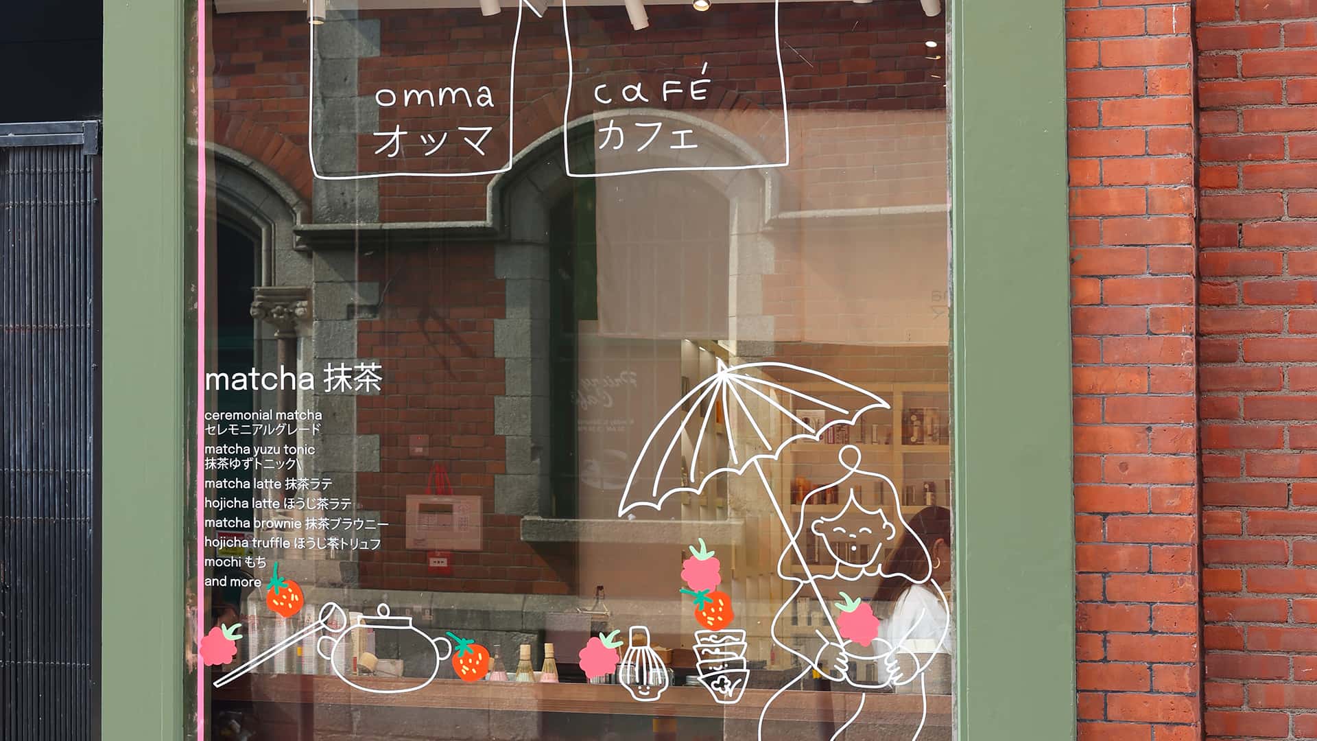 A café window with handwritten signs, illustrations of a person with an umbrella, and strawberry graphics.