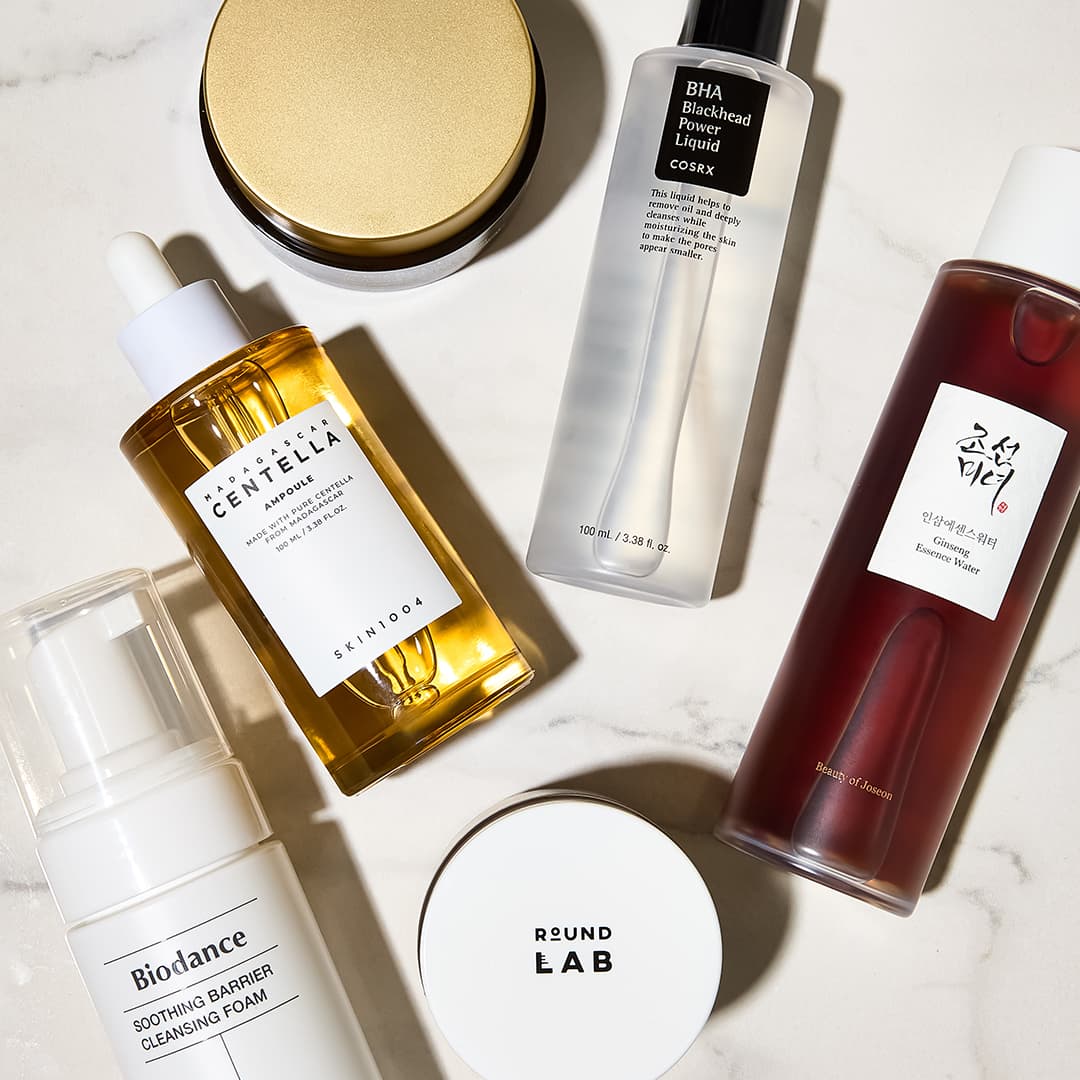 Skincare products arranged on a light surface, including serums, cleansing foam, and containers with various labels.