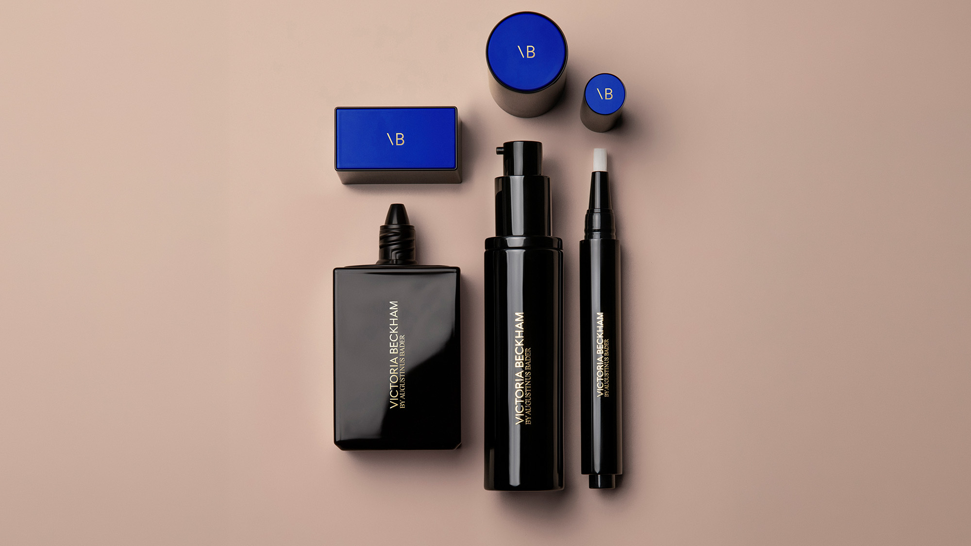 Victoria Beckham beauty collection with blue compacts, black fragrance bottle, facial mist and eyeshadow pen on beige background