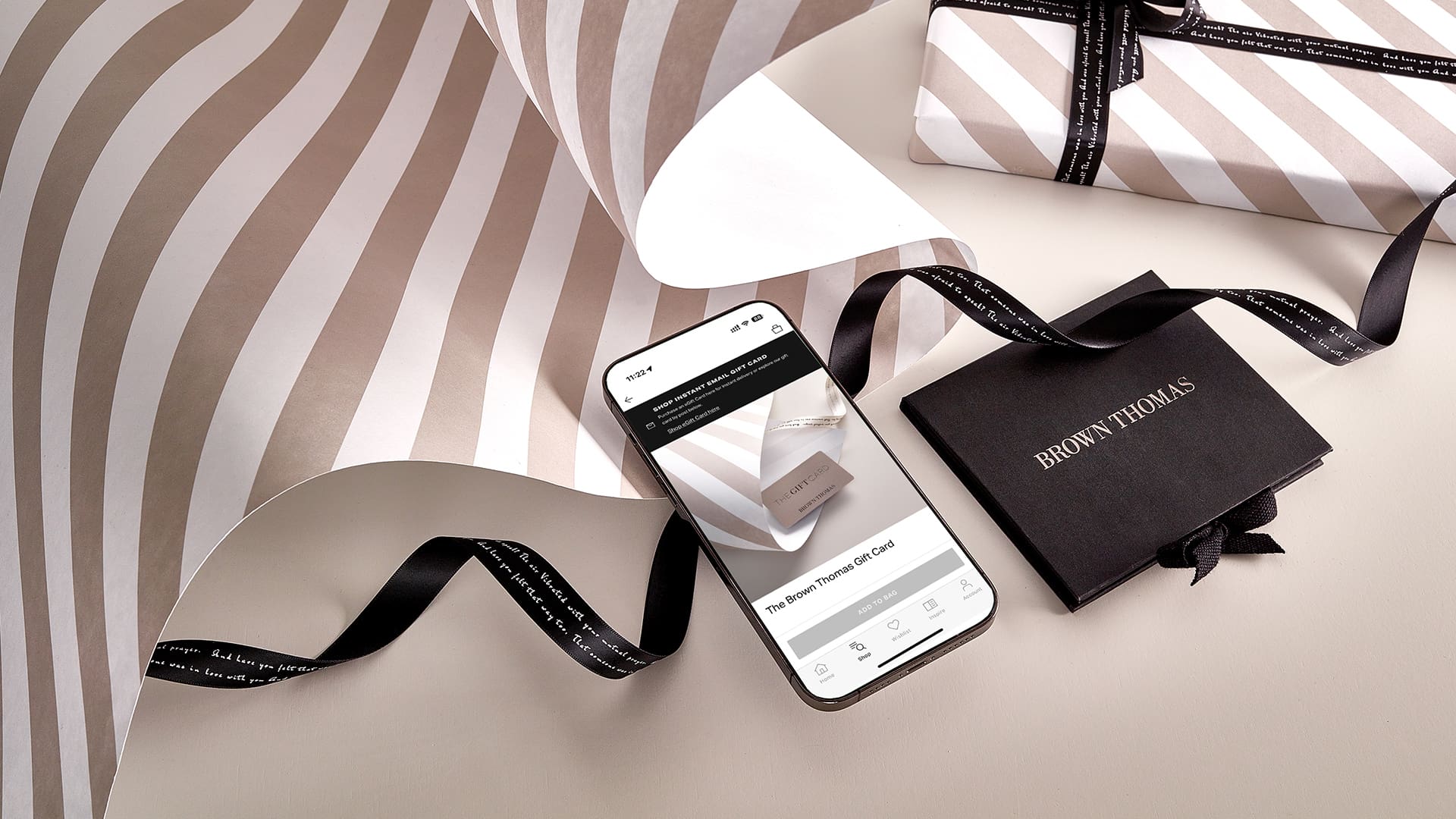 A smartphone displaying a website lies beside striped wrapping paper, a wrapped gift, and a black gift box with a ribbon.