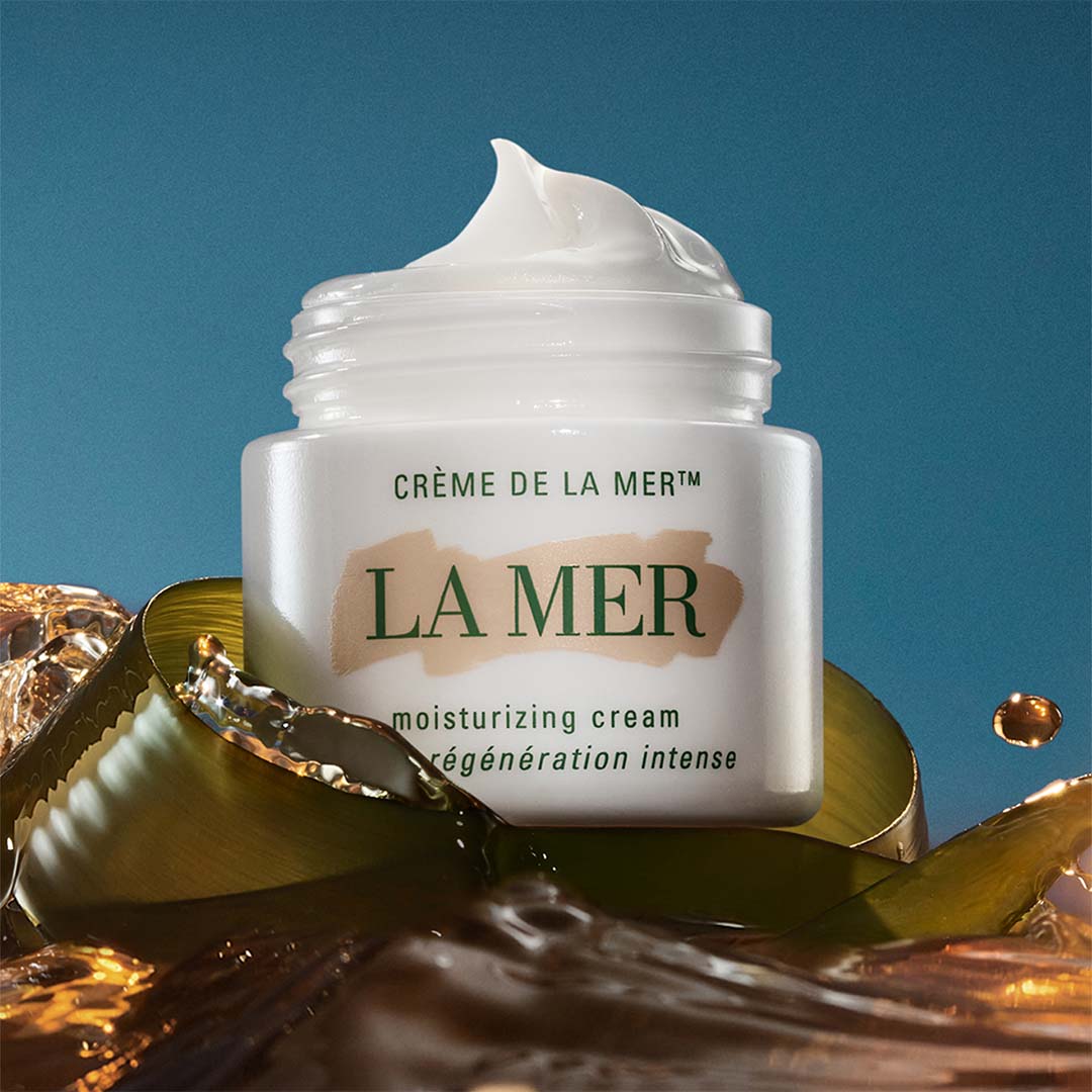 A jar of La Mer moisturizing cream with its lid off, surrounded by a shimmering background.