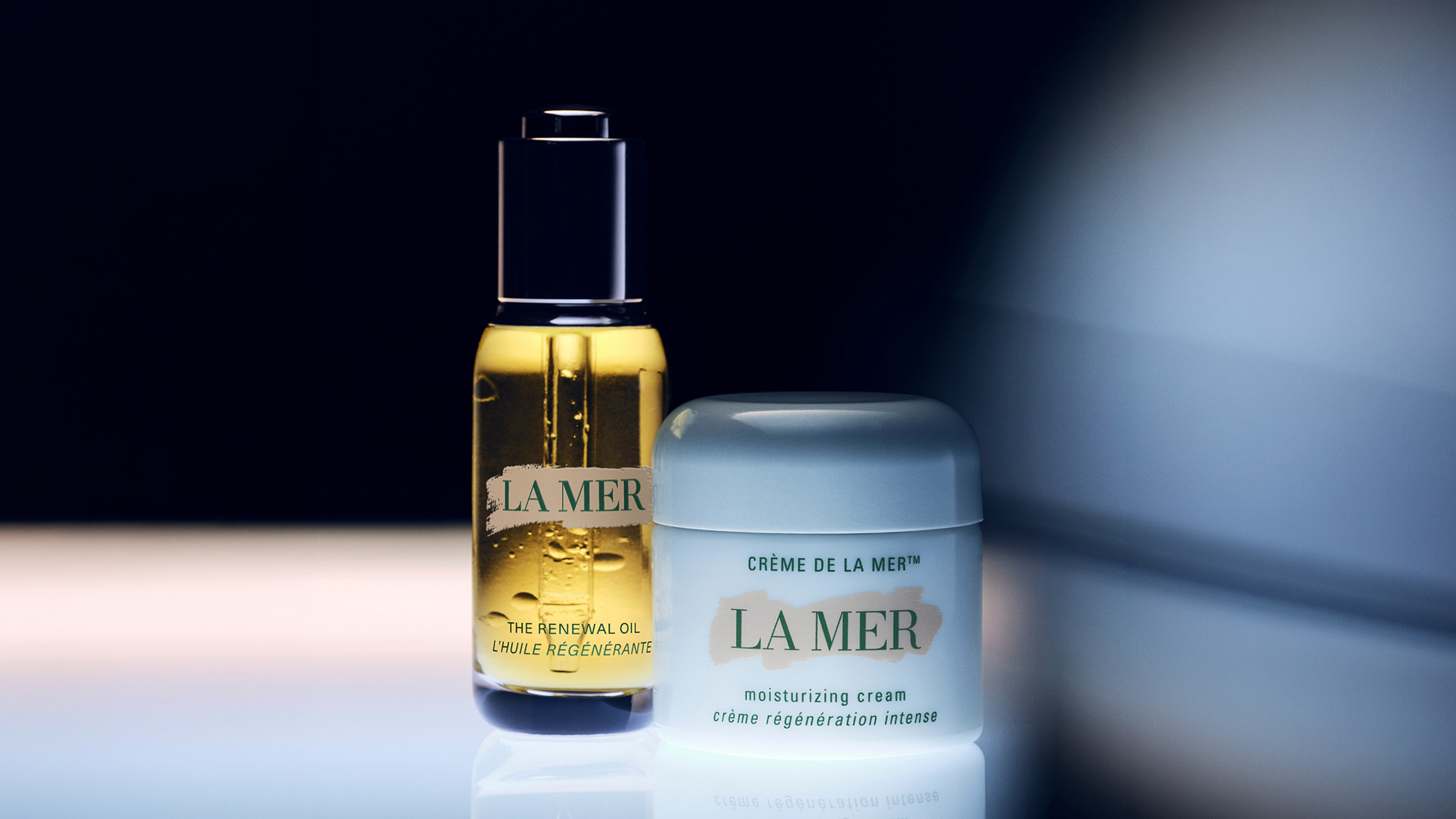 La Mer skincare featuring the renewal oil and moisturising cream on reflective surface against dark background