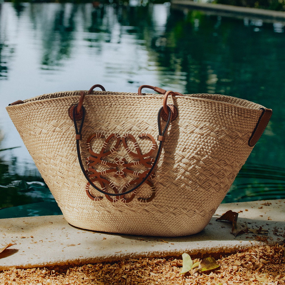 Woven straw tote bag with brown leather handles displayed by a tranquil waterside setting