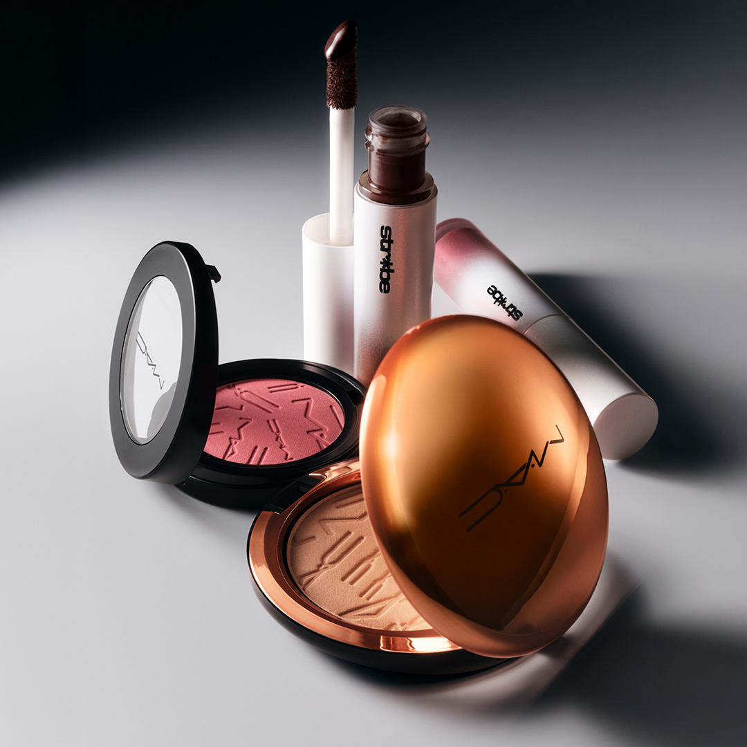 MAC makeup collection featuring eyeshadow palette, lipstick, liquid eyeliner and bronzer compact on neutral background