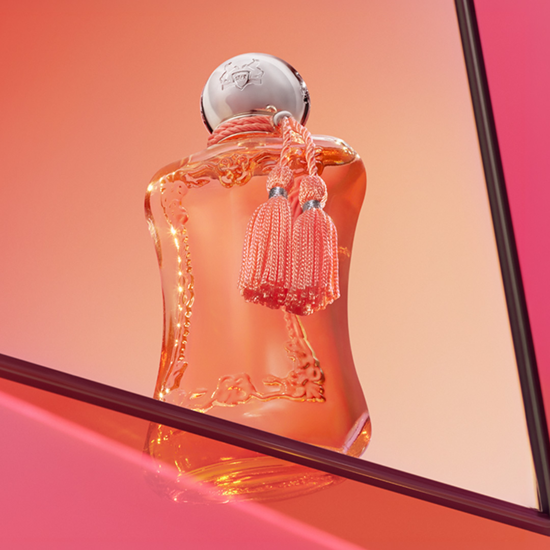 Ornate orange perfume bottle with decorative tassel and silver cap on pink gradient background