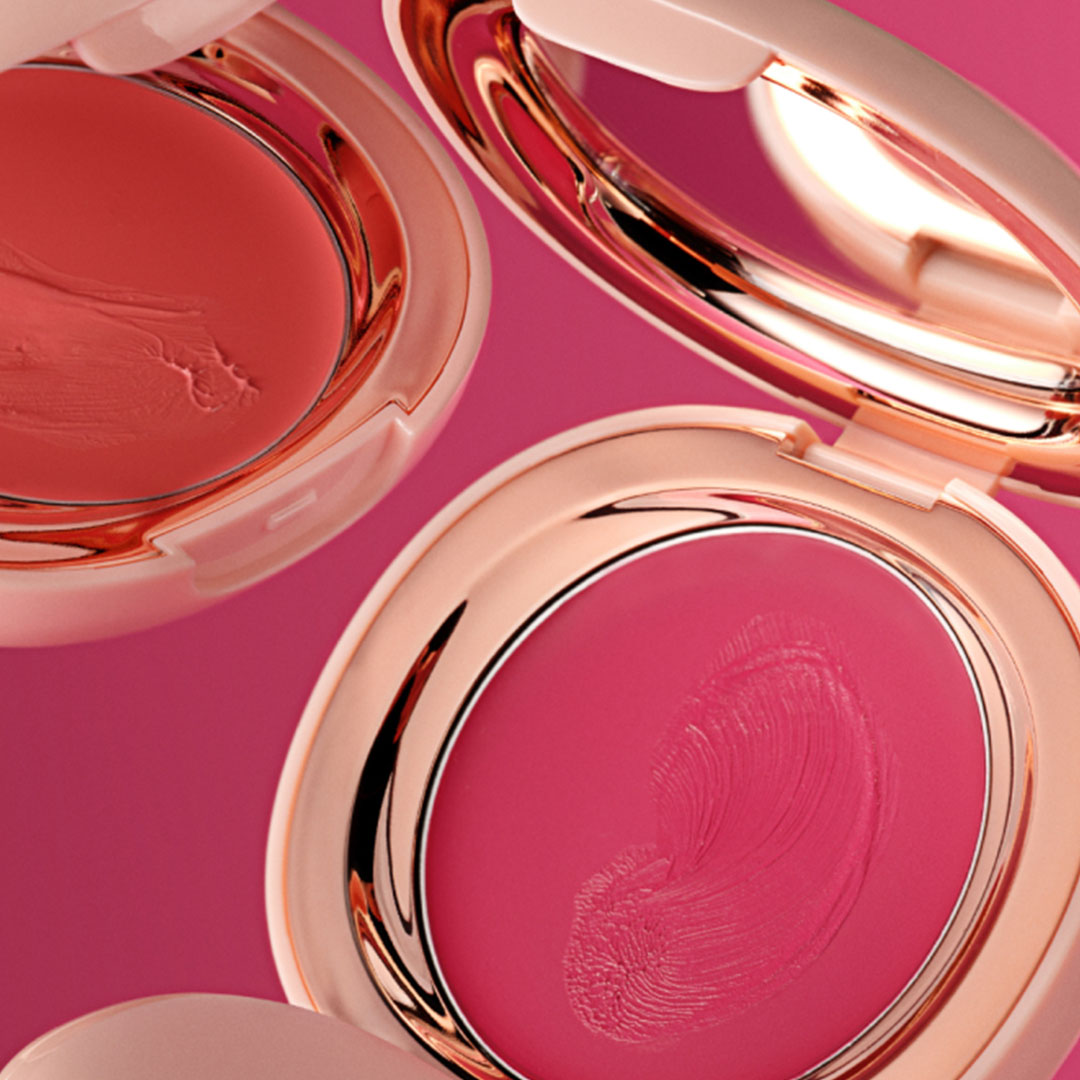 Three open cream blush compacts in coral and pink shades on a vibrant pink background