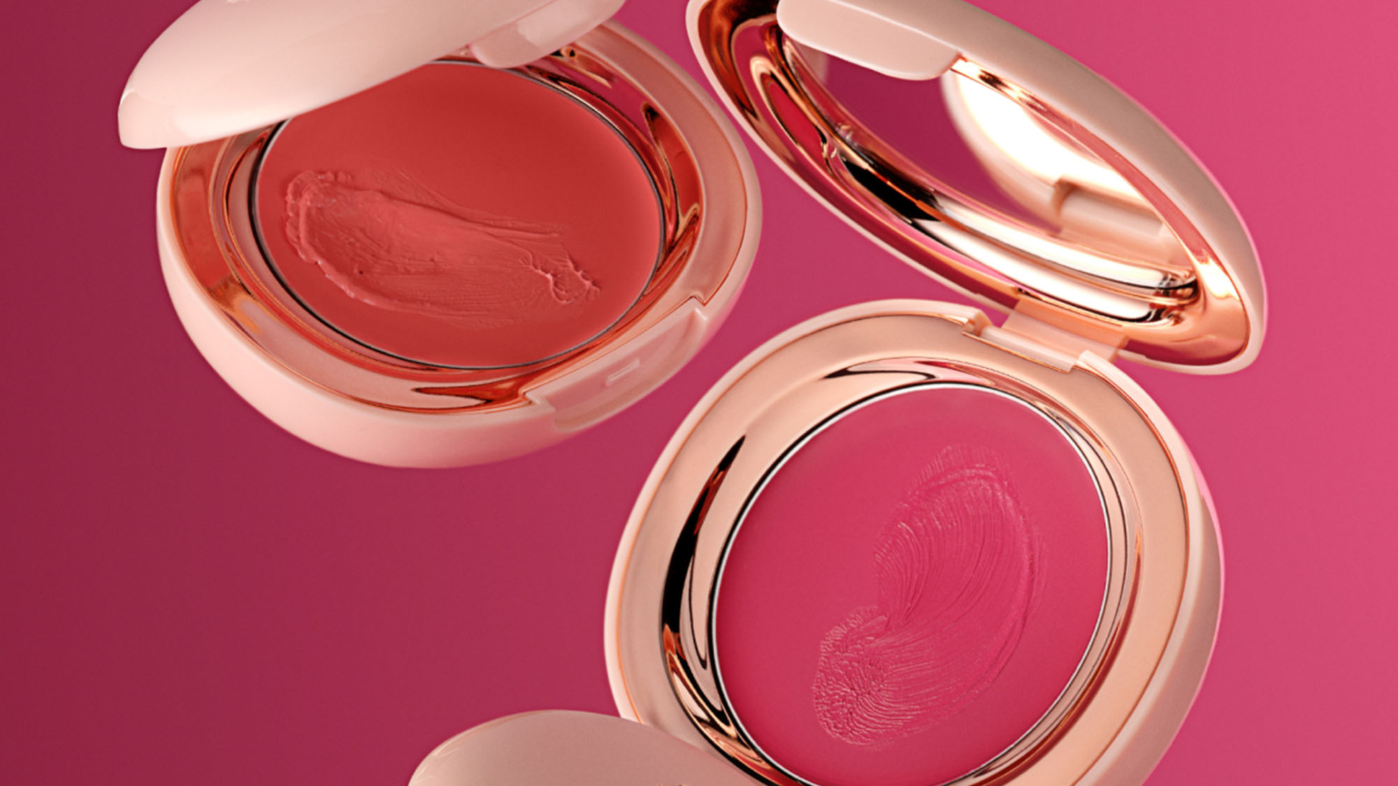 Three open cream blush compacts in coral and pink shades on a vibrant pink background