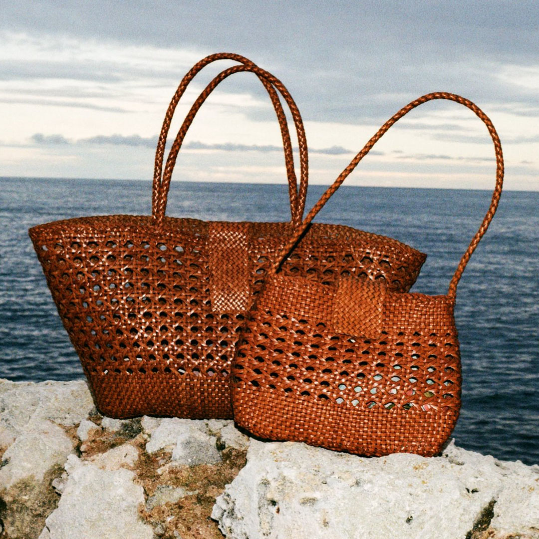 Two rust-coloured open-weave tote bags with handles on white stone overlooking sea