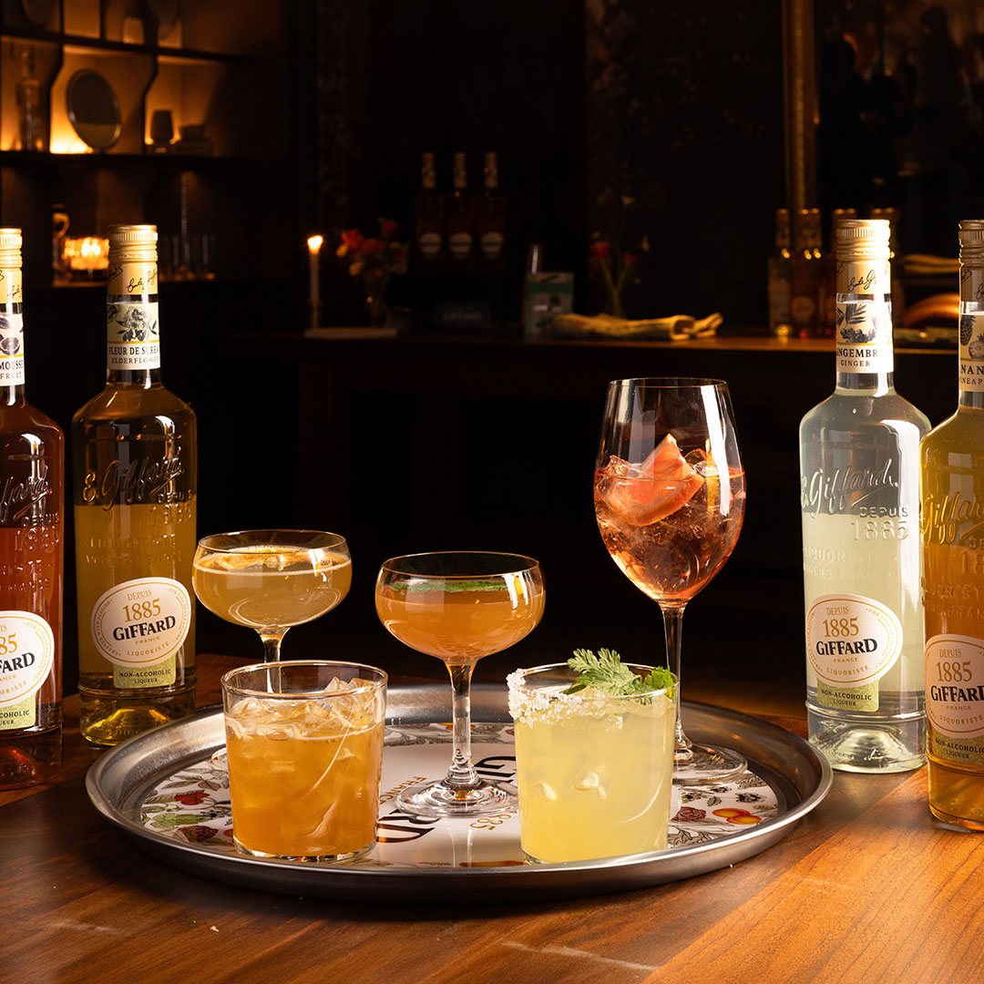 Giffard liqueur bottles with assorted cocktails on decorative tray in evening setting