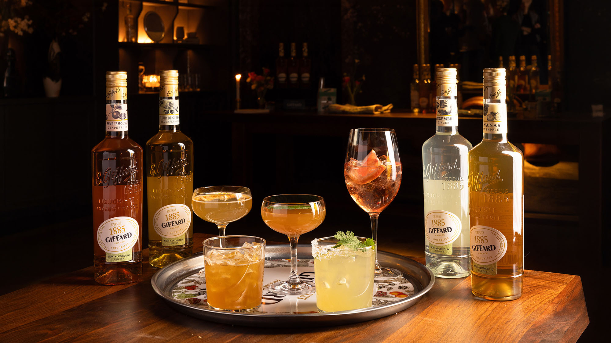 Giffard liqueur bottles with assorted cocktails on decorative tray in evening setting
