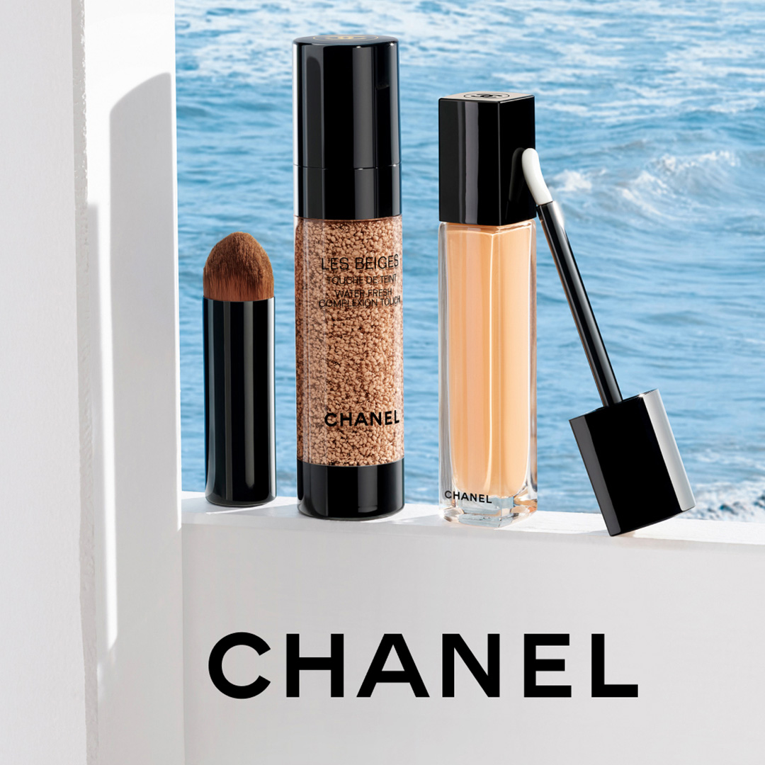 Chanel Les Beiges makeup collection featuring lipstick, water-resistant powder, and concealer displayed against sea and sky background