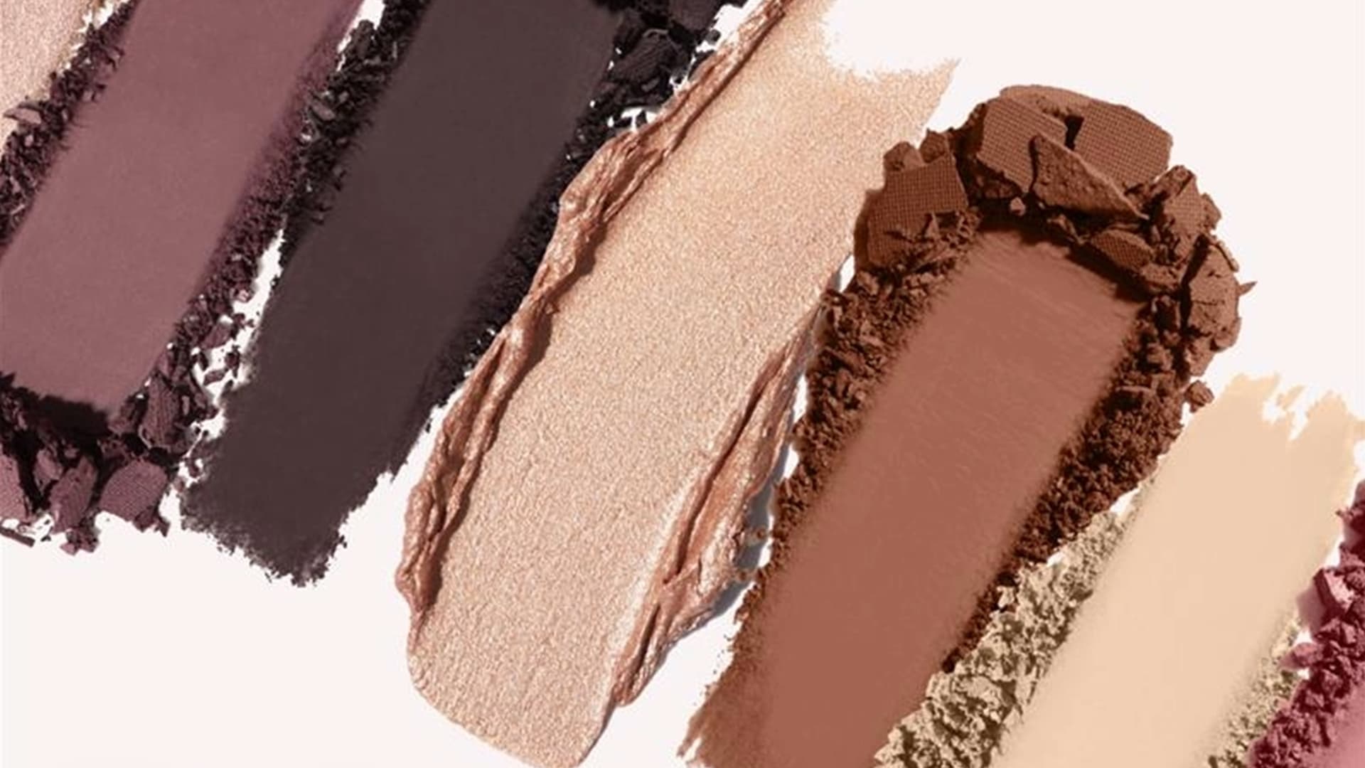 Swatches of eyeshadow and powder cosmetics in neutral and warm brown tones displayed diagonally