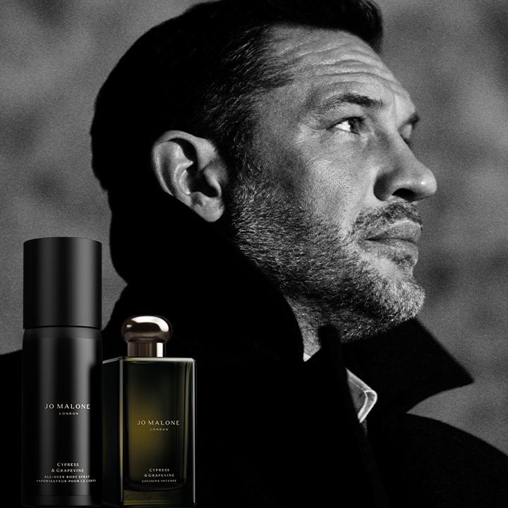 A man in profile wearing a coat with Jo Malone's Cypress & Grapevine fragrance bottles in the foreground.