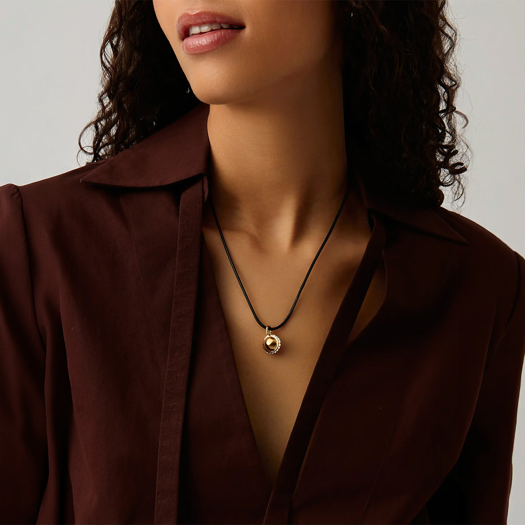 Woman wearing burgundy blazer and gold pendant necklace on black cord