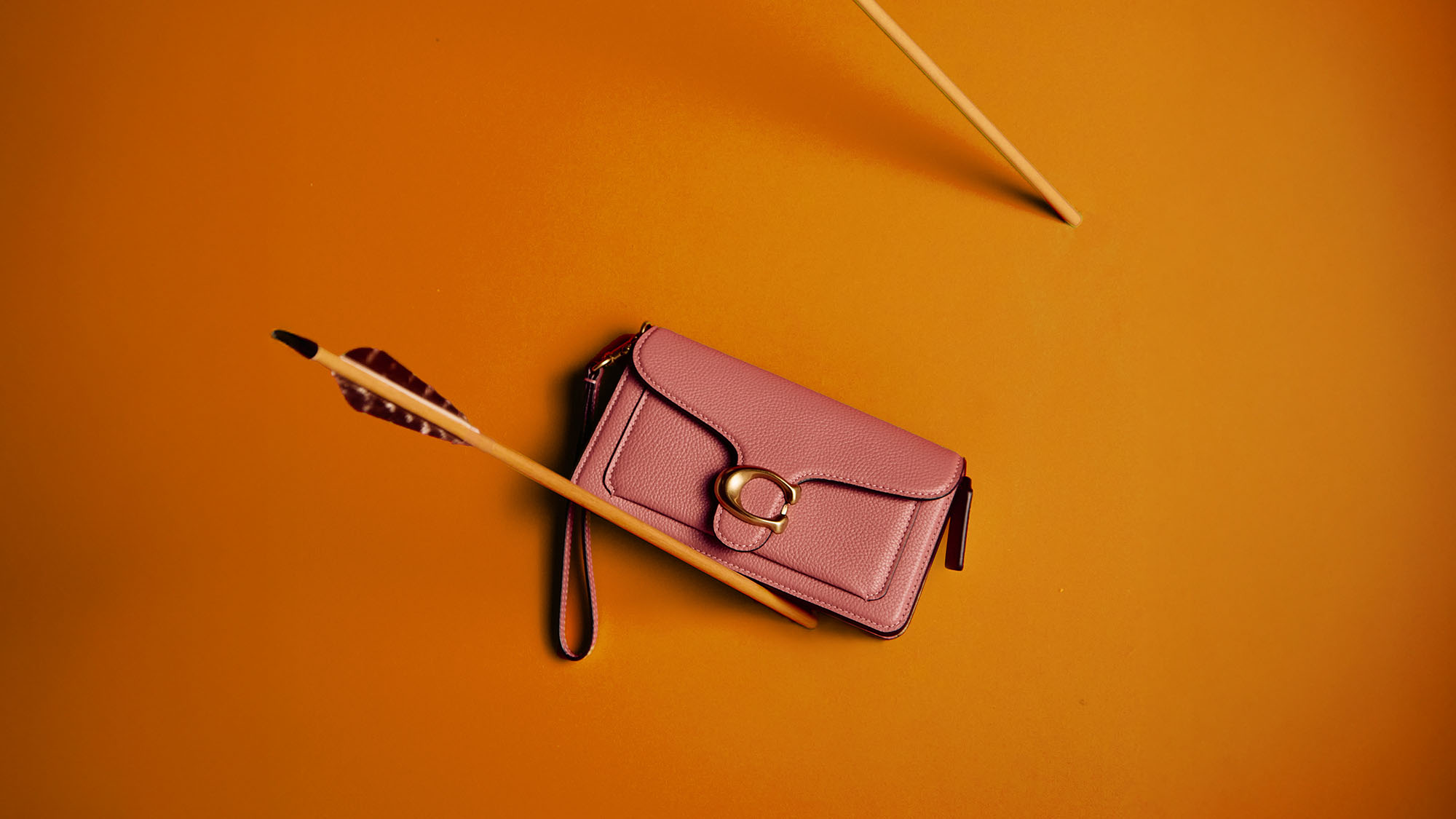 A black handbag with a gold chain hangs on a red wall, pierced by several arrows.