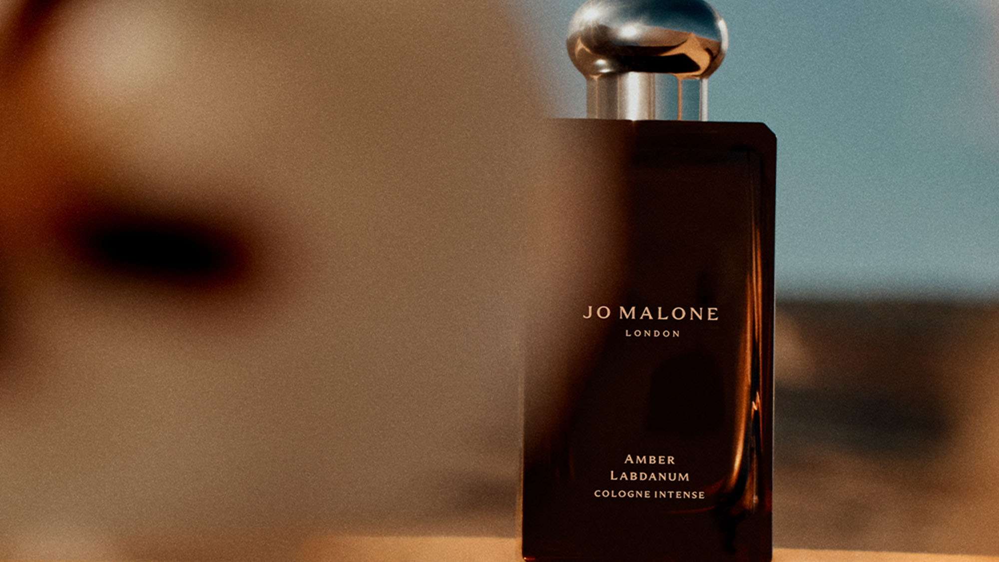A bottle of Jo Malone London Amber & Labdanum cologne against a blurred background.