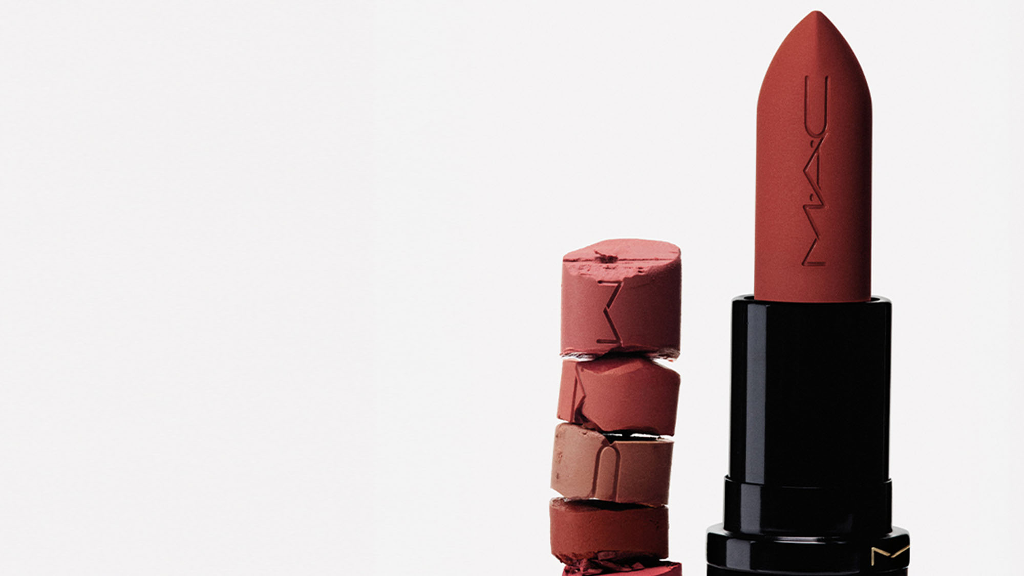 A MAC lipstick with a broken stack of lipstick pieces beside it on a white background.