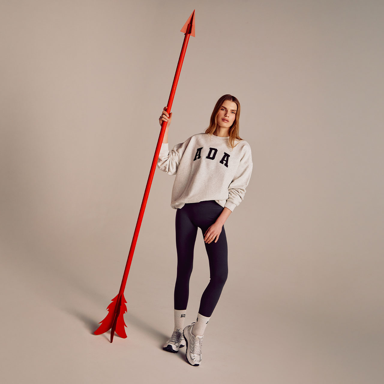A person in a white 'ADA' sweatshirt and black leggings holds a tall red pole.