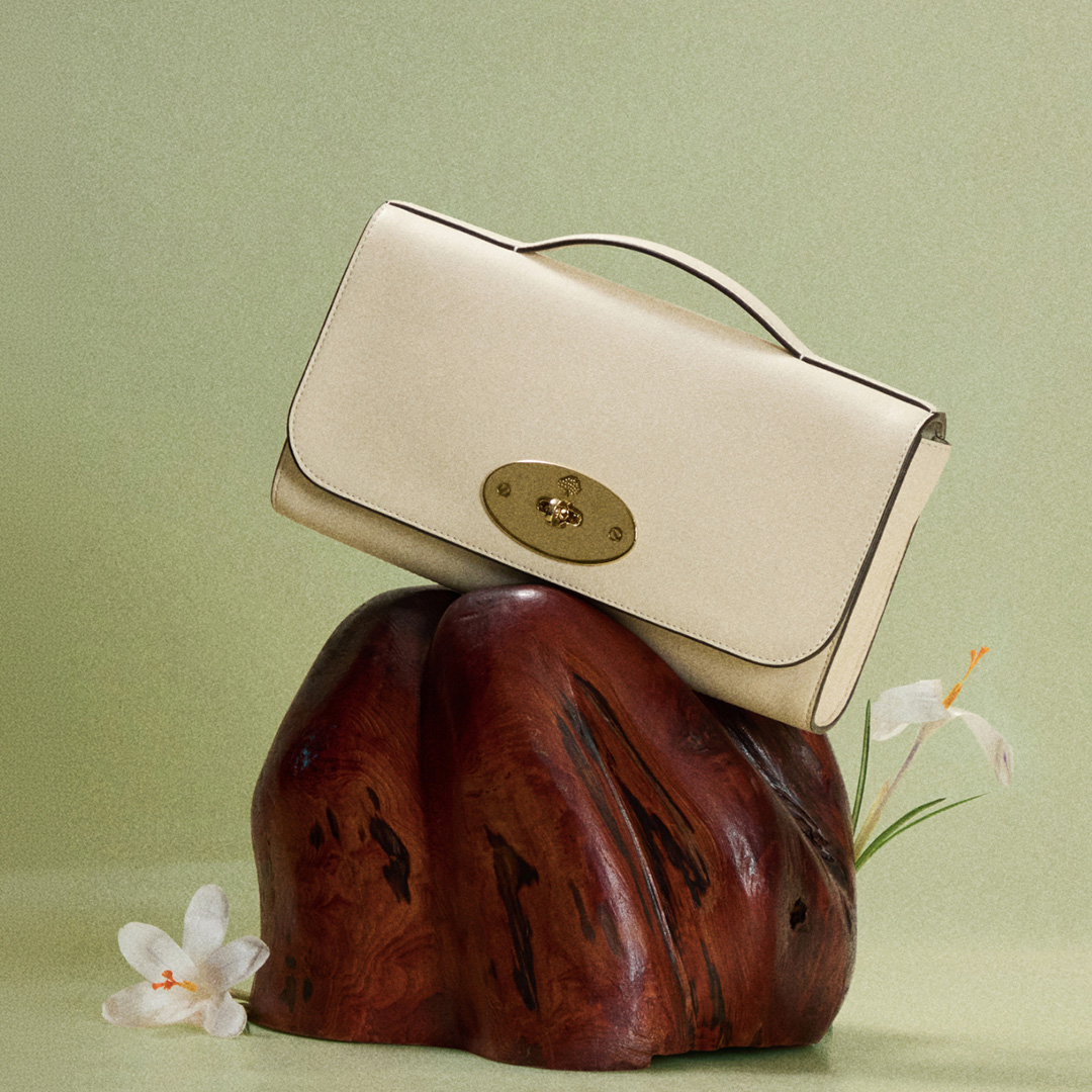 Cream leather structured handbag with gold clasp displayed on dark wood form with white flowers