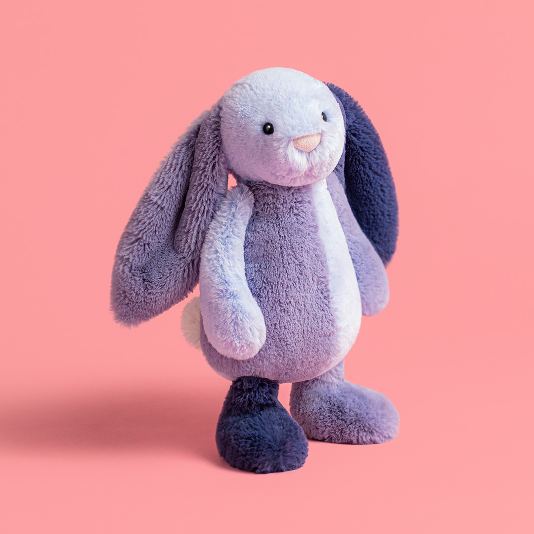 Soft purple and white plush bunny toy with long ears against a pink background
