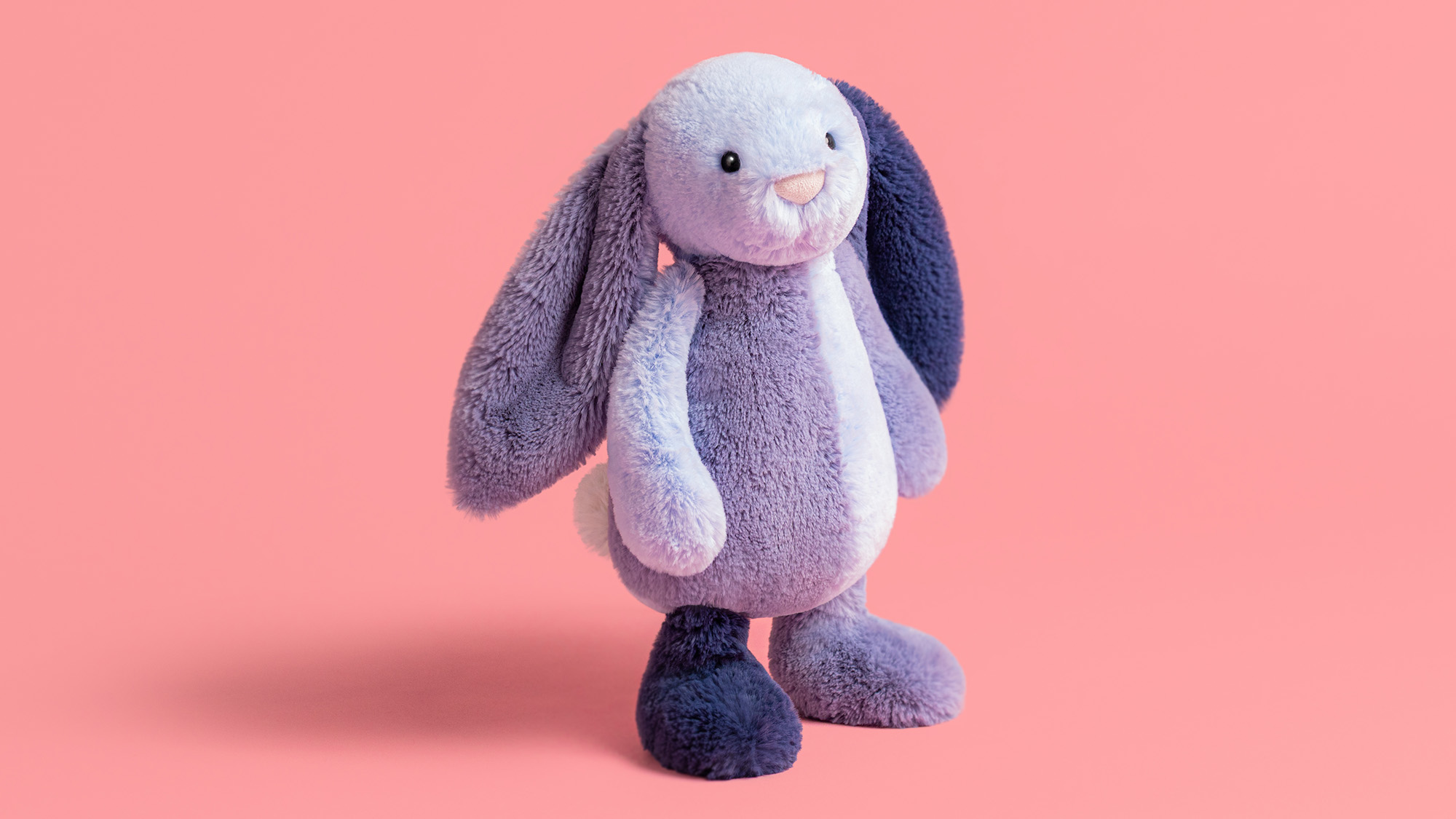 Soft purple and white plush bunny toy with long ears against a pink background