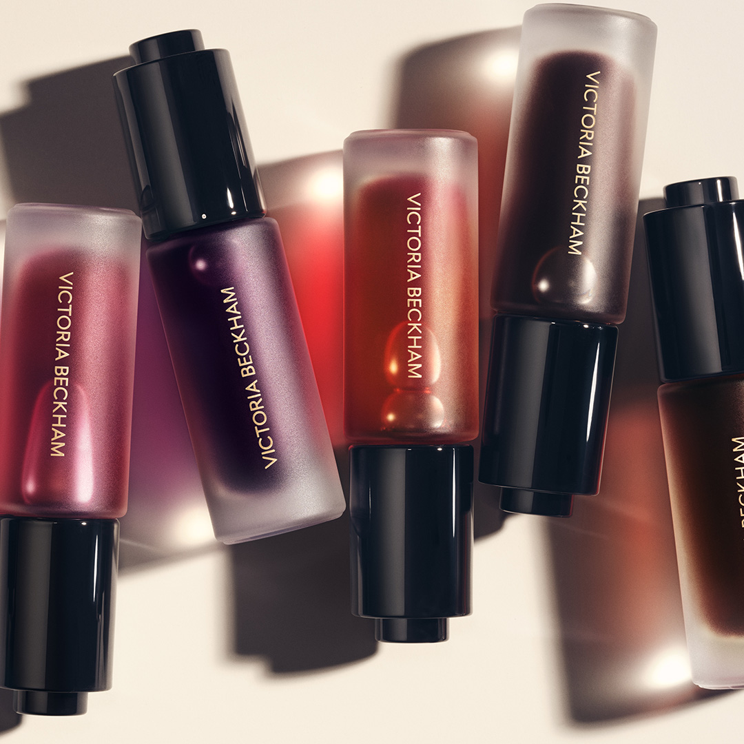 Victoria Beckham Beauty Colour Wash range displaying six liquid pigment bottles in warm burgundy, rose, and bronze shades