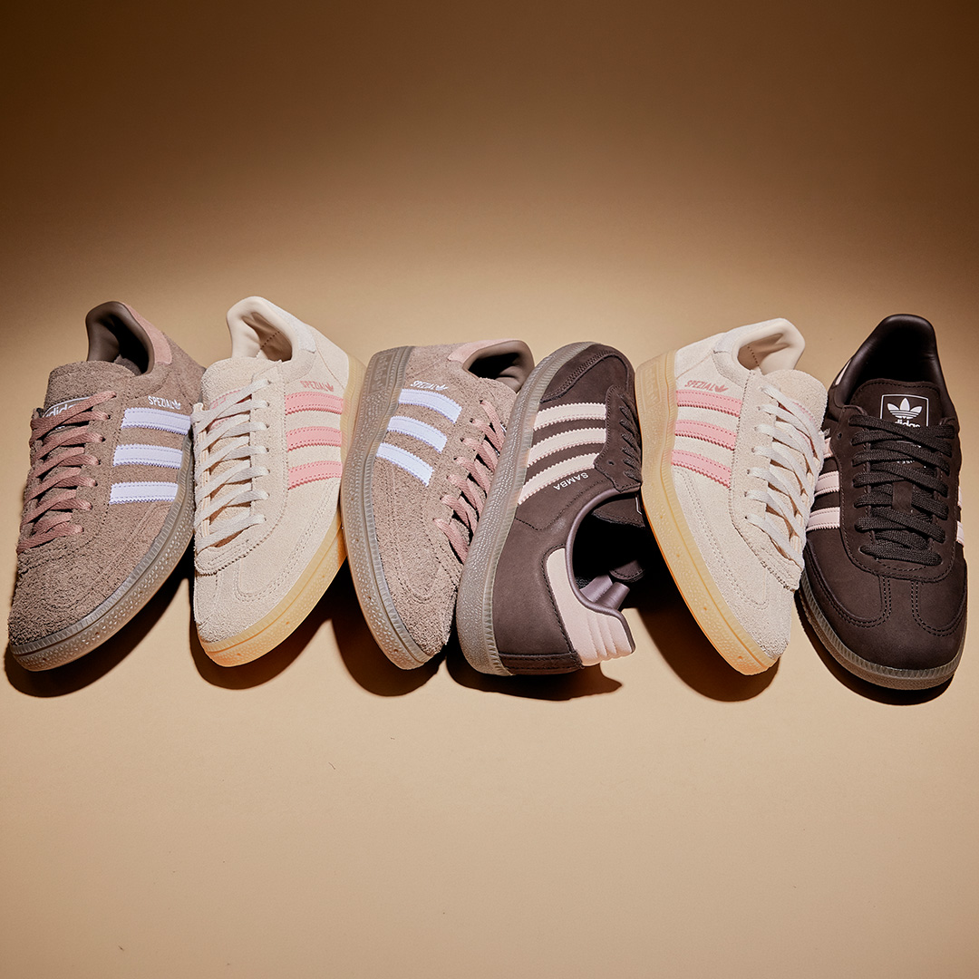 Collection of Adidas trainers in neutral tones including cream, pink, brown and white, displayed against a beige background
