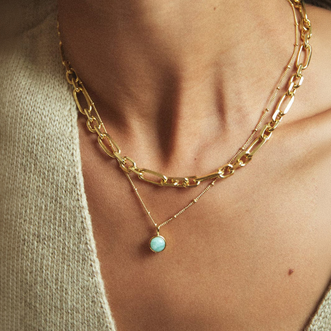 Woman wearing layered gold chain necklaces with turquoise pendant in cream knit top
