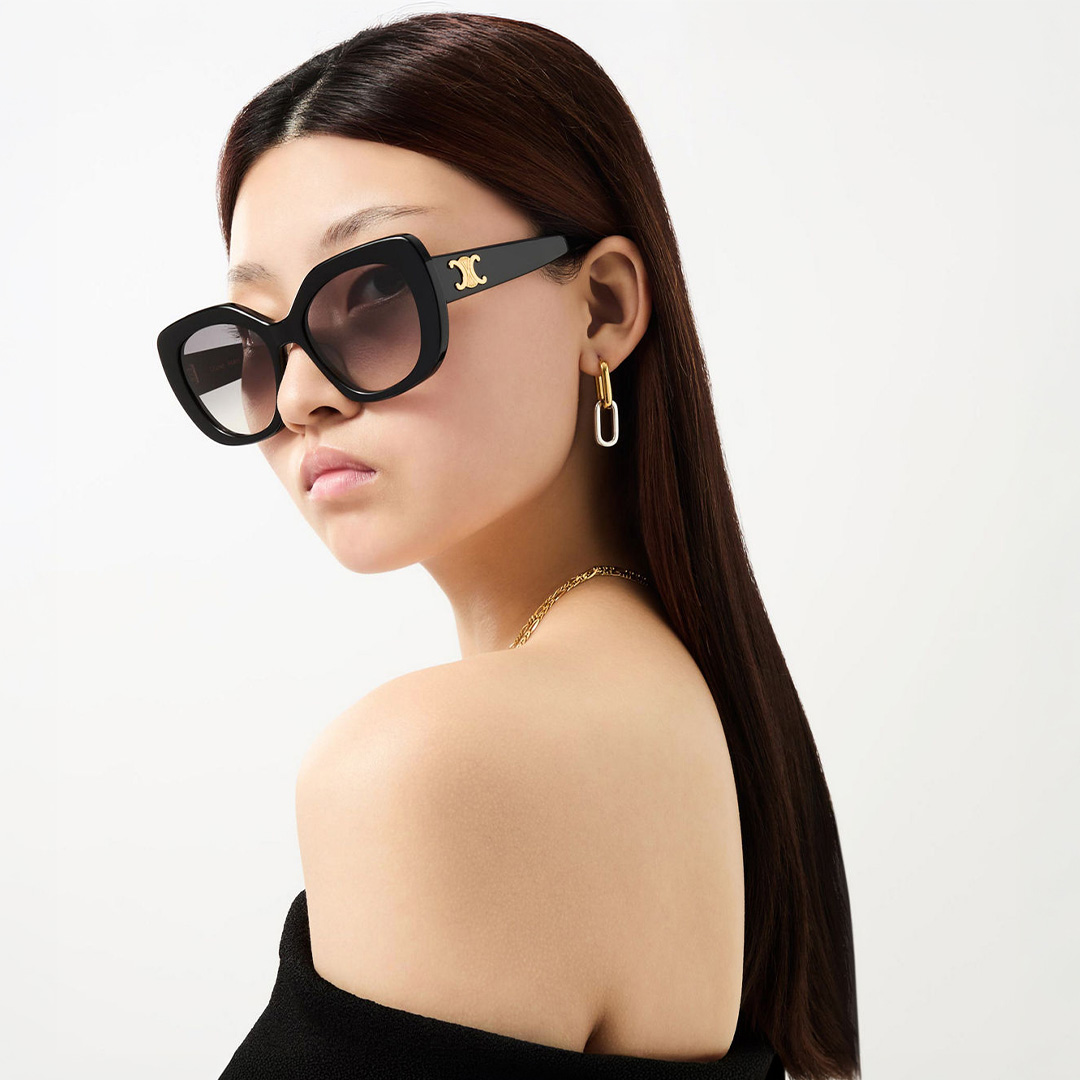 Woman wearing oversized black sunglasses with gold accents and gold hoop earrings