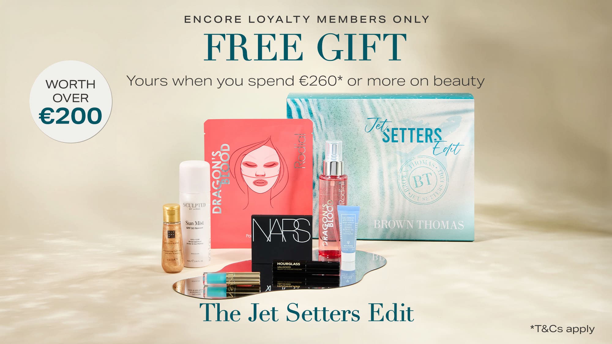 A promotional image showing a collection of beauty products, including a red box, NARS item, and other cosmetics, arranged in front of a turquoise package labelled 'The Jet Setters Edit'. Text reads: “Encore Loyalty Members Only. Free Gift. Yours when you spend €260* or more on beauty. Worth over €200.” Terms and conditions apply.