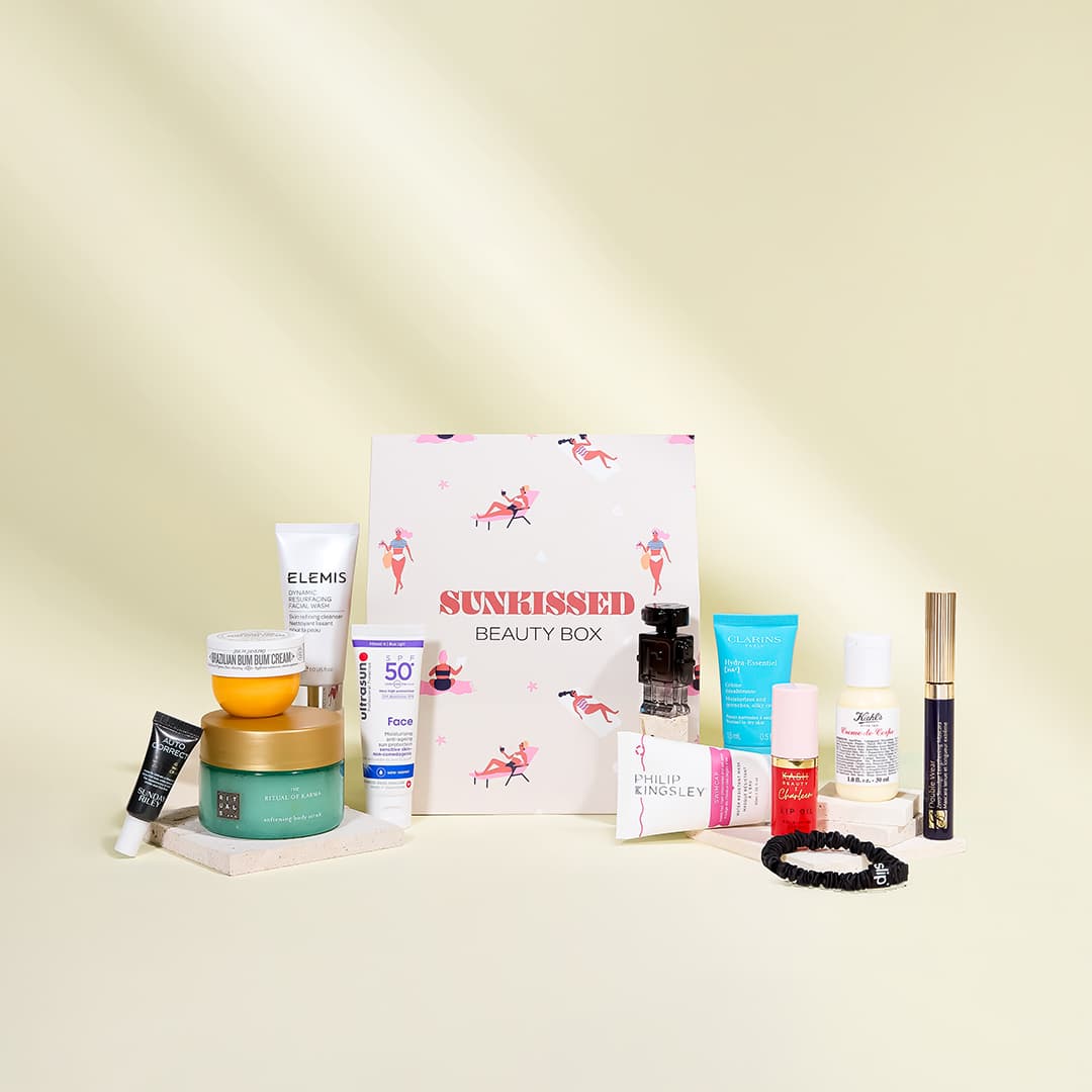 A collection of beauty products displayed around an open box labelled 'Sunkissed Beauty Box' on a light yellow background. The assortment includes skincare creams, lotions, sunscreen, a hair product, a tube of mascara, a small pink bottle, and a black scrunchie, showcasing a variety of brands.