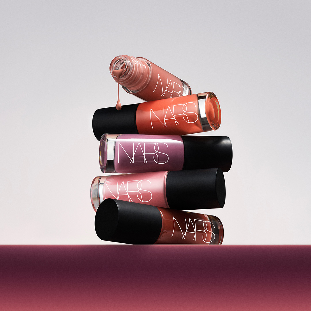 Stack of five NARS Insatiable liquid blush bottles in varying shades of pink, coral, and burgundy with black caps
