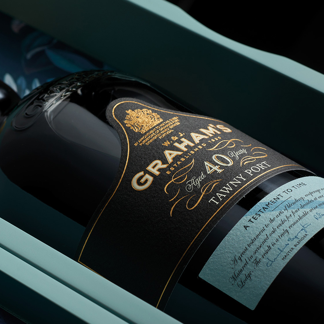 Bottle of Graham's aged port wine with black label and gold lettering displayed against teal background
