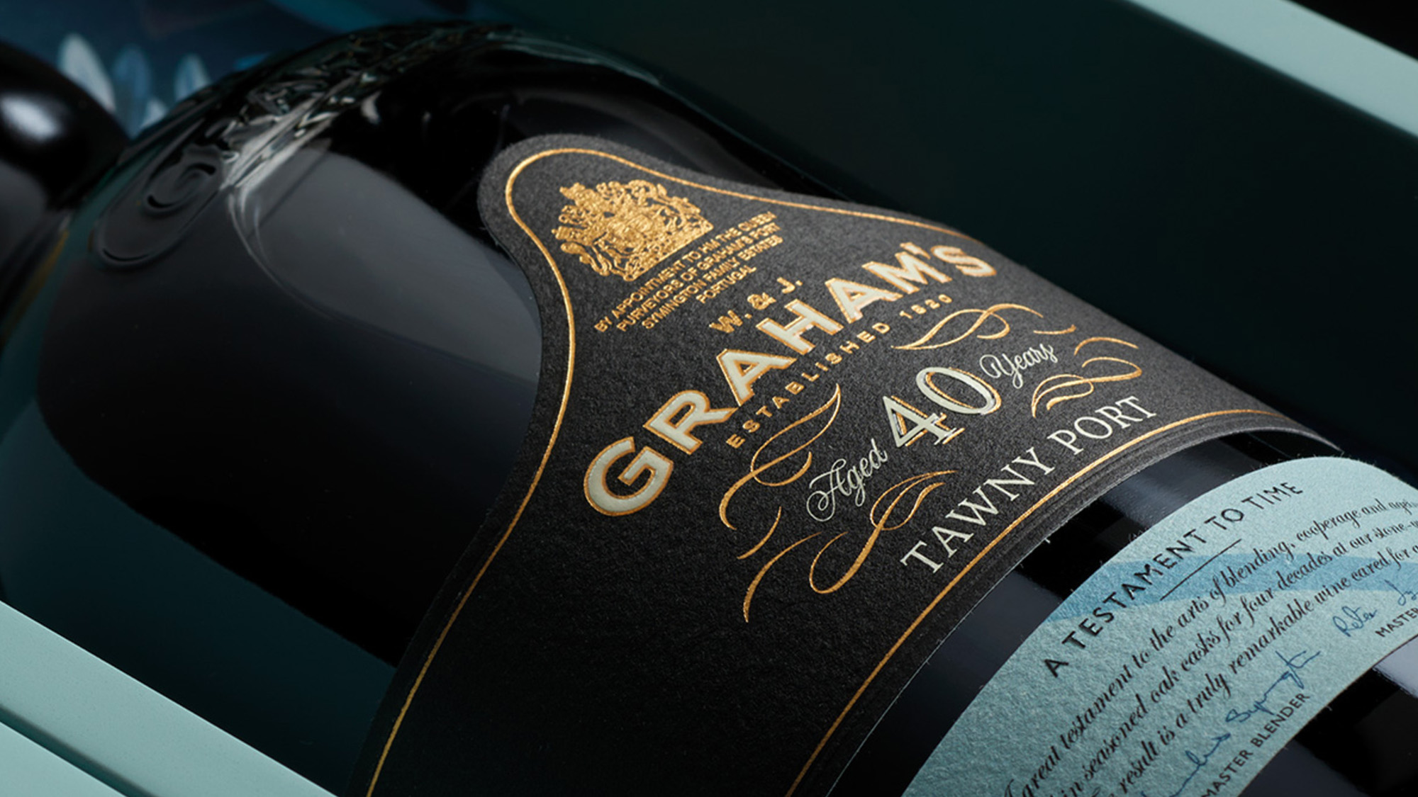 Bottle of Graham's aged port wine with black label and gold lettering displayed against teal background