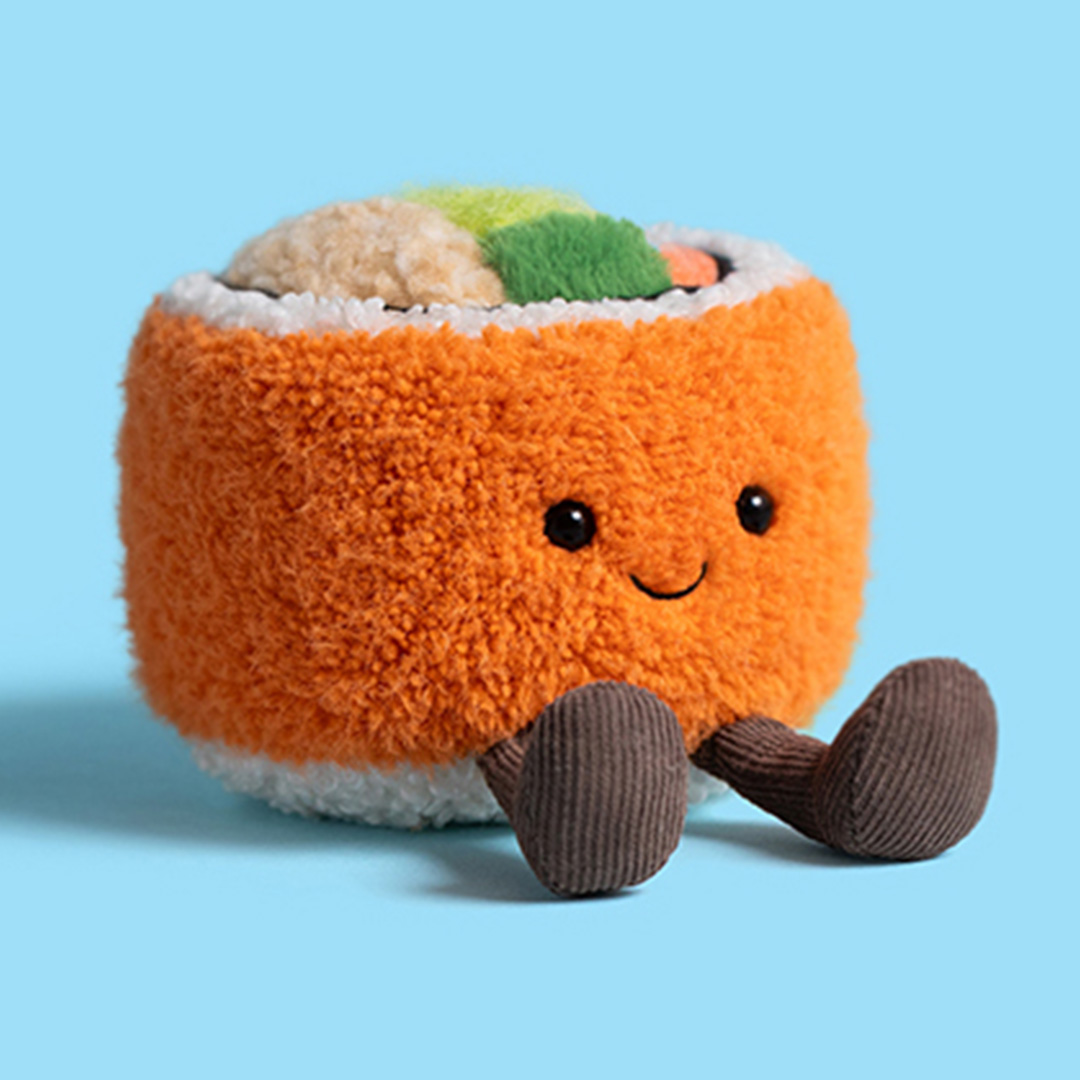 Orange plush Jellycat toy character with smiling face and brown legs, holding multicoloured sushi-shaped toys on light blue background
