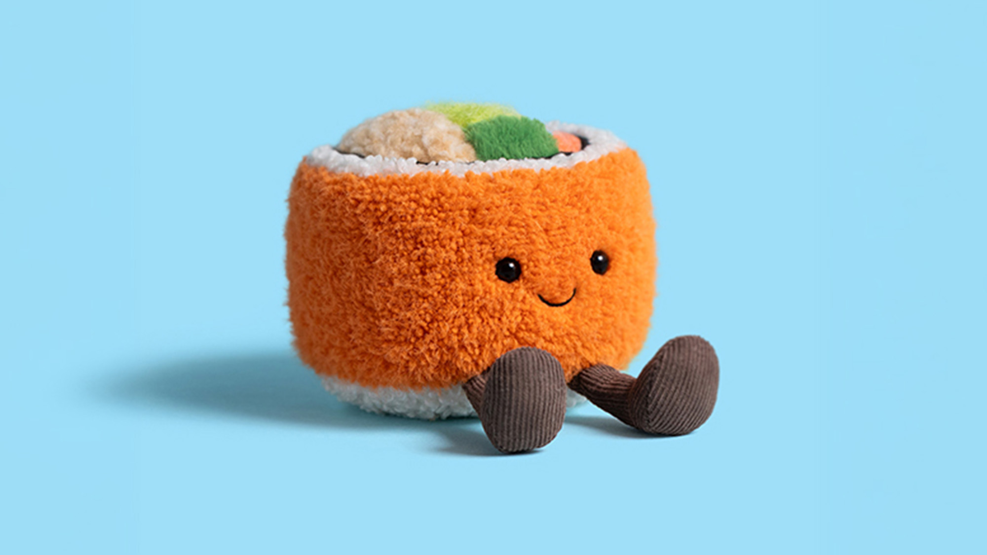 Orange plush Jellycat toy character with smiling face and brown legs, holding multicoloured sushi-shaped toys on light blue background