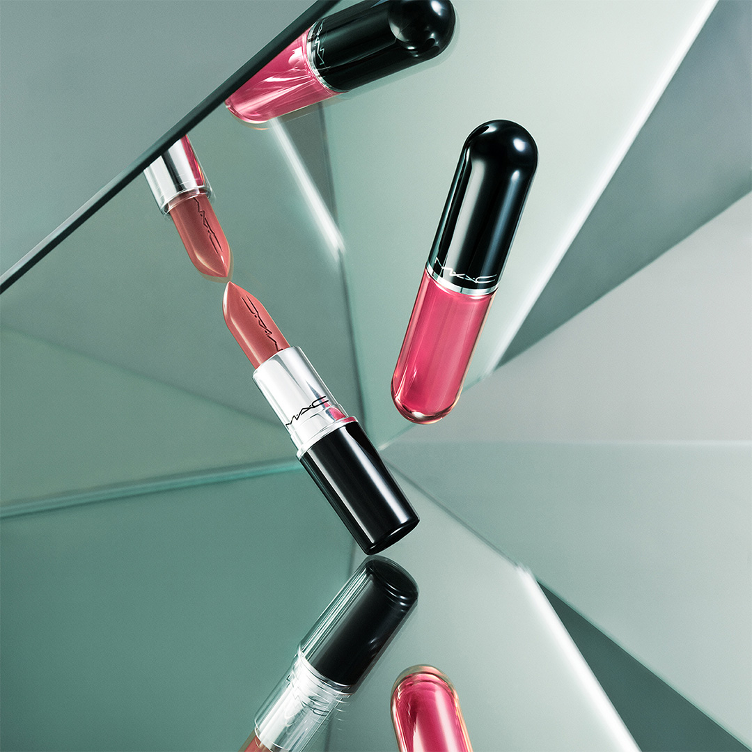 Arrangement of Lustreglass lipsticks and lip glosses in pink and burgundy shades with reflective finish on split tonal background