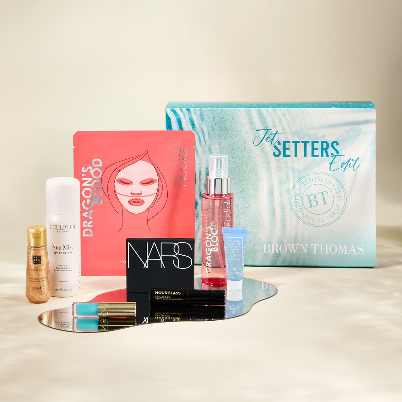 Curated beauty gift set with branded boxes, cosmetics, and skincare products displayed on reflective surface, Jet Setters Edit packaging