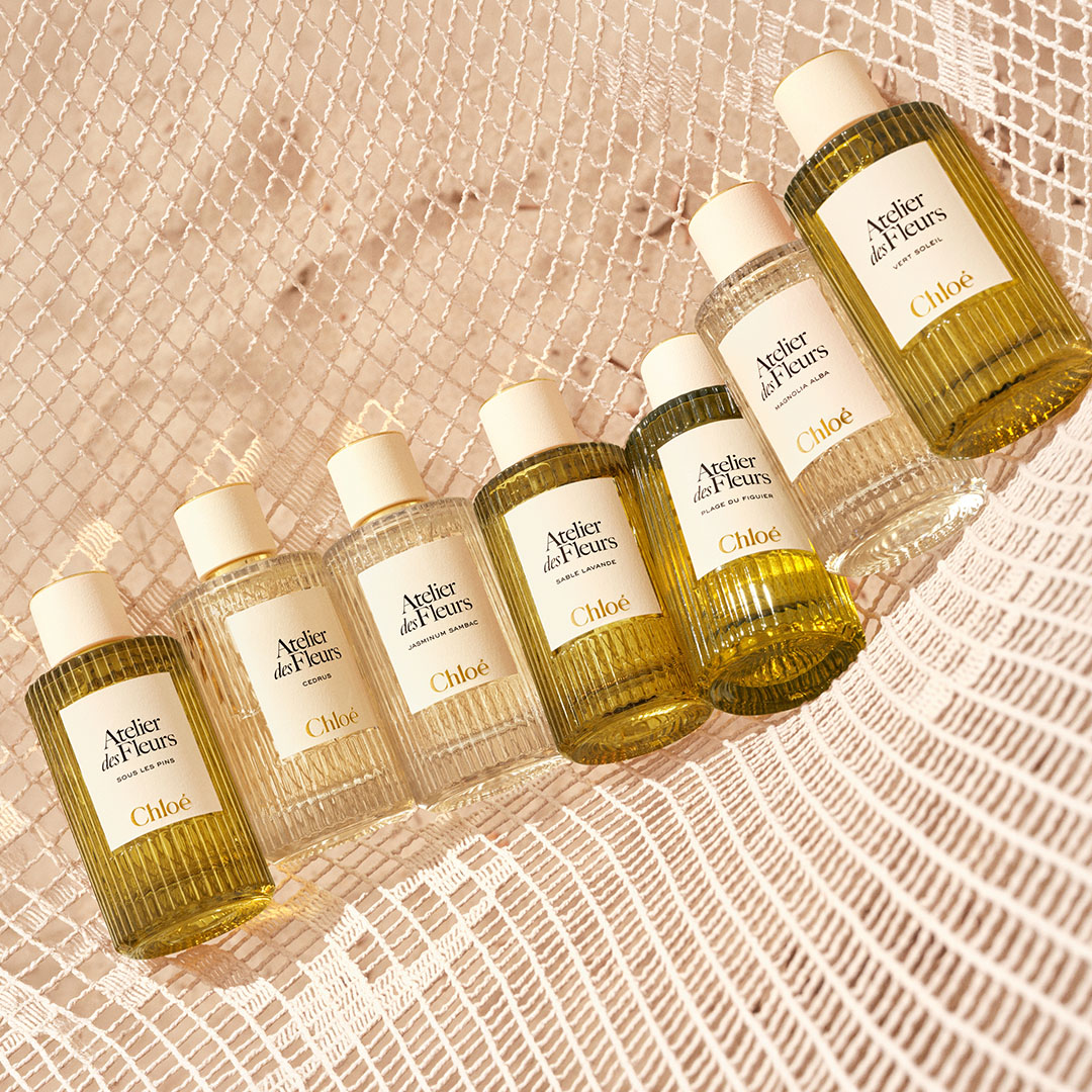Six Chloé Atelier des Fleurs fragrance bottles arranged diagonally on textured beige background