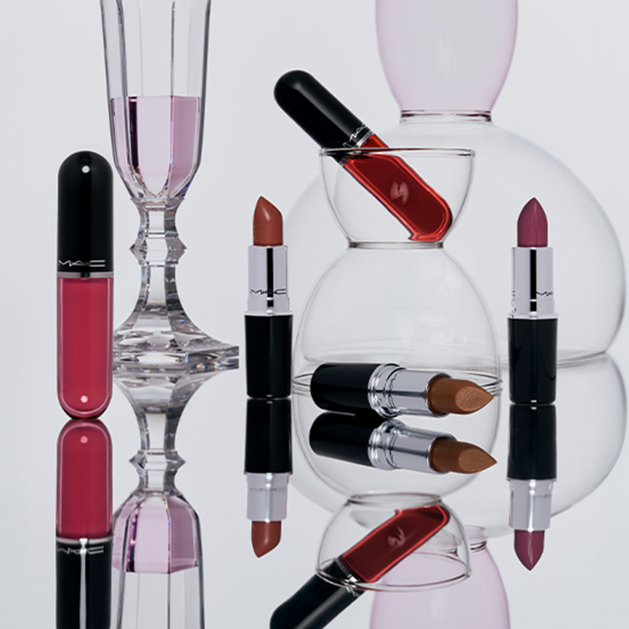 M.A.C Lustreglass Sheer-Shine Lipsticks and Stainglass Lip Tints in various shades with glass vessels and liquid colour swatches