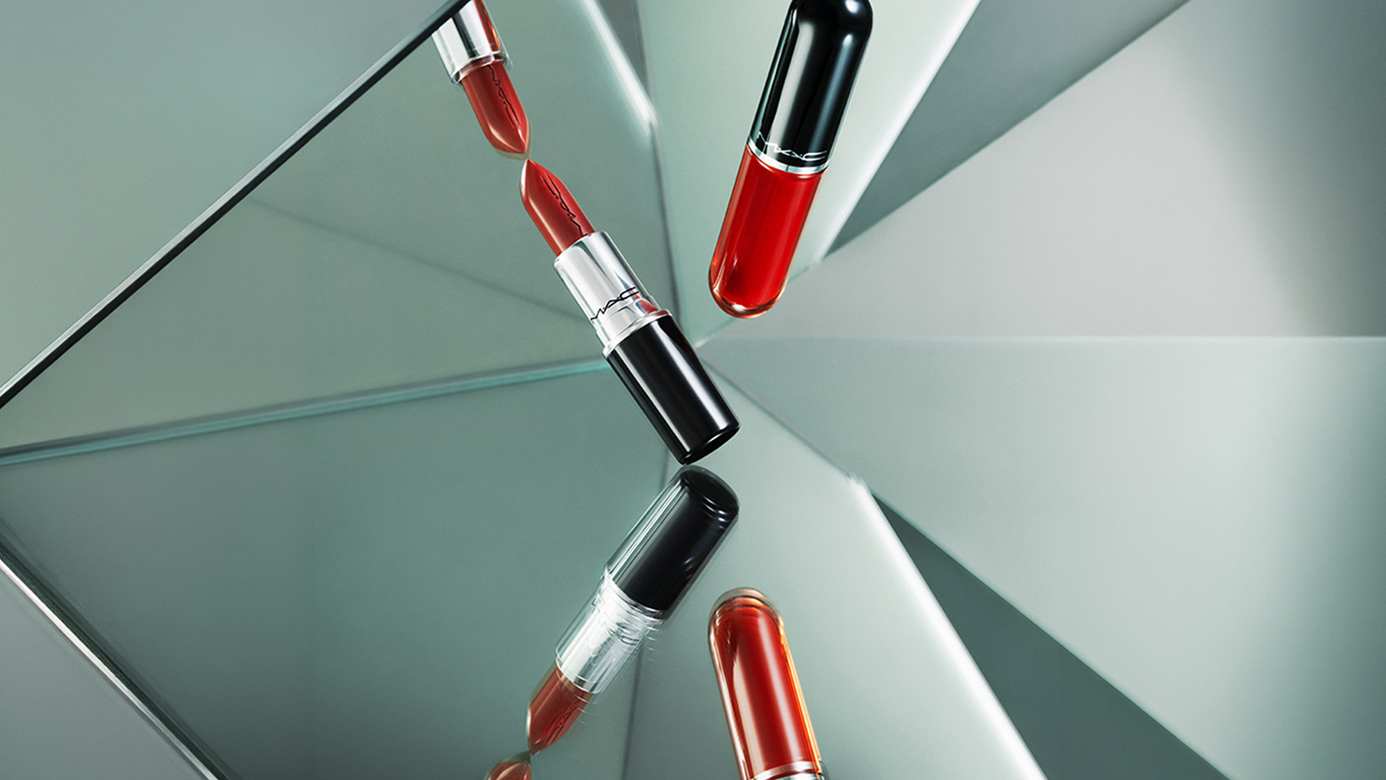 M.A.C Lustreglass lipsticks in red shades arranged on geometric mint green surface