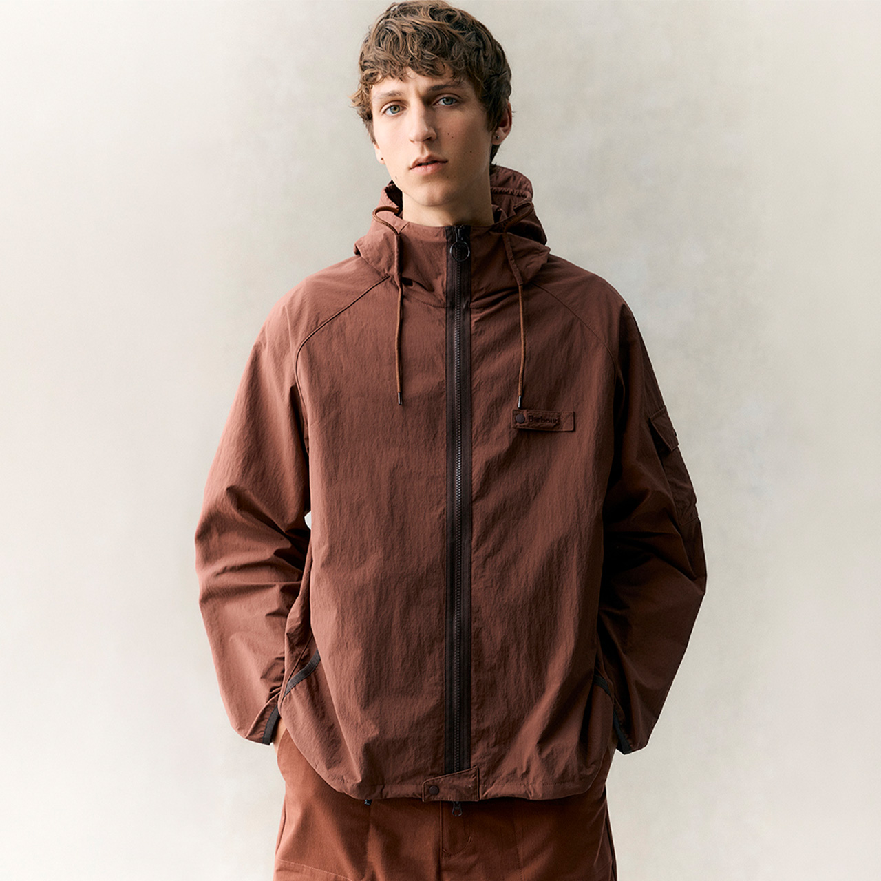 Young man wearing rust-brown hooded jacket with zip fastening against neutral background