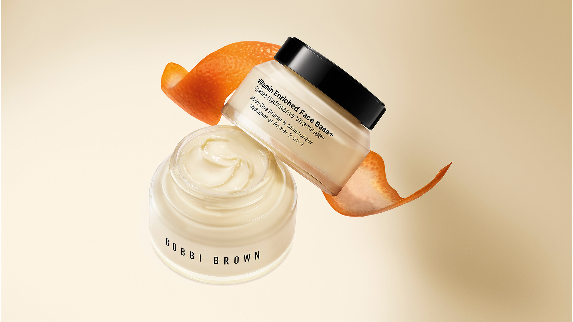 Bobbi Brown Vitamin Enriched Face Base with cream texture and orange peel garnish on beige background